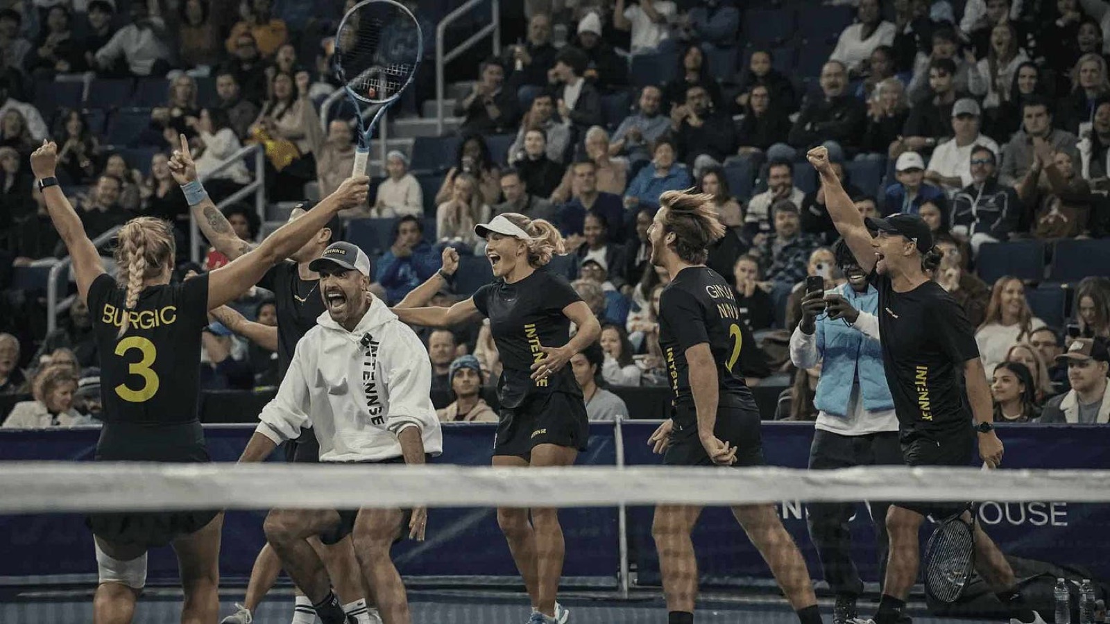 An INTENNSE team celebrating together at the net in front of a packed arena crowd.